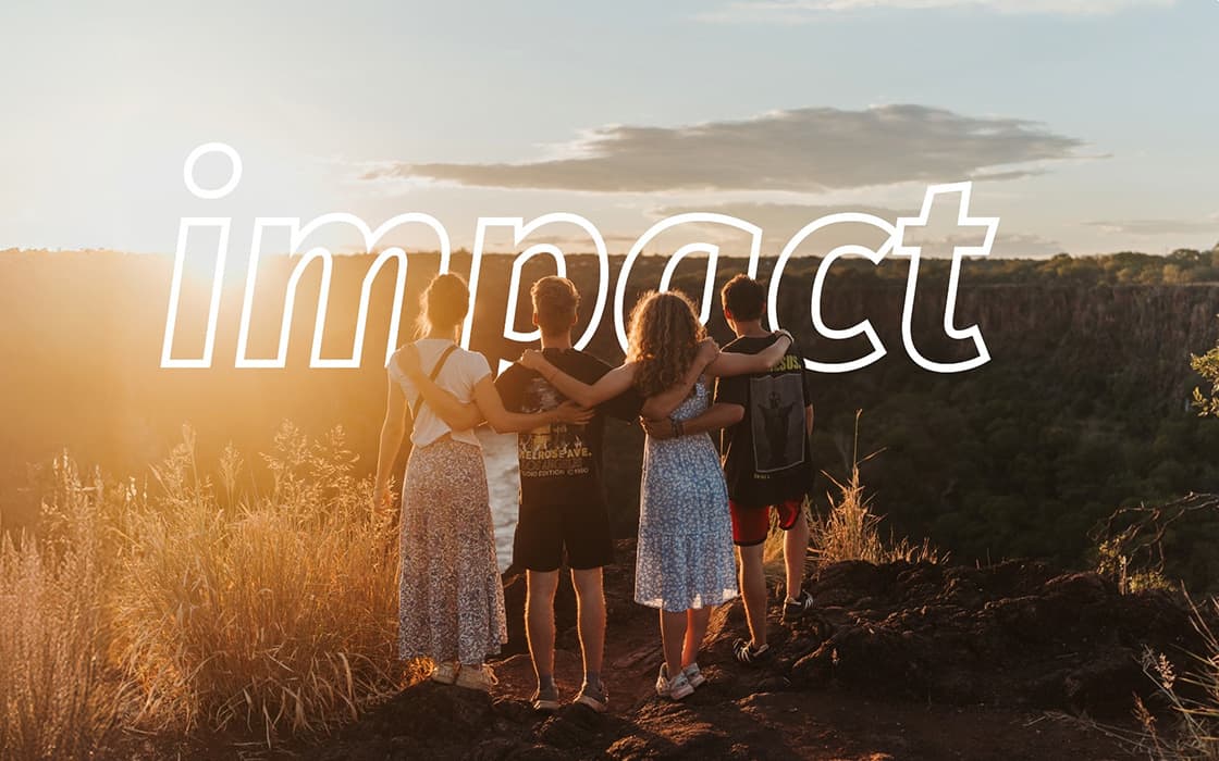 Vier Personen, die sich in den Armen liegen, stehen bei Sonnenuntergang auf einem Hügel, wobei das Wort impact über das Bild gelegt ist.