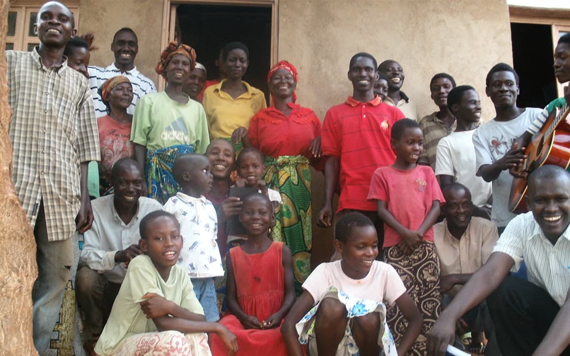 Eine große Gruppe von Menschen, darunter Kinder und Erwachsene, lächelt vor einem Gebäude von Projekt Leben in Burundi.