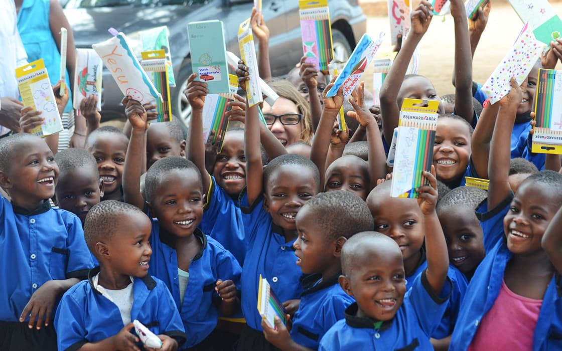 Lächelnde Kinder in blauen Uniformen halten Schulmaterial hoch, das von Projekt Leben in Burundi unterstützt wird.