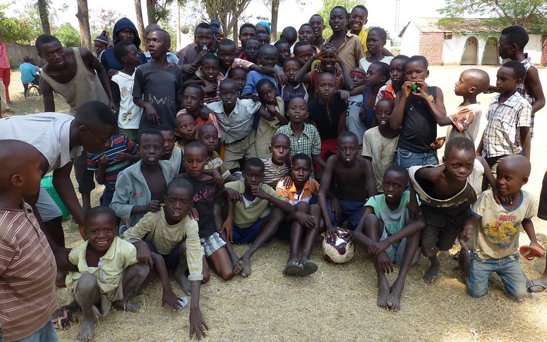 Eine große Gruppe lächelnder Kinder und Jugendlicher von Projekt Leben BAHO versammelt sich im Freien auf trockenem Gras für ein Foto.