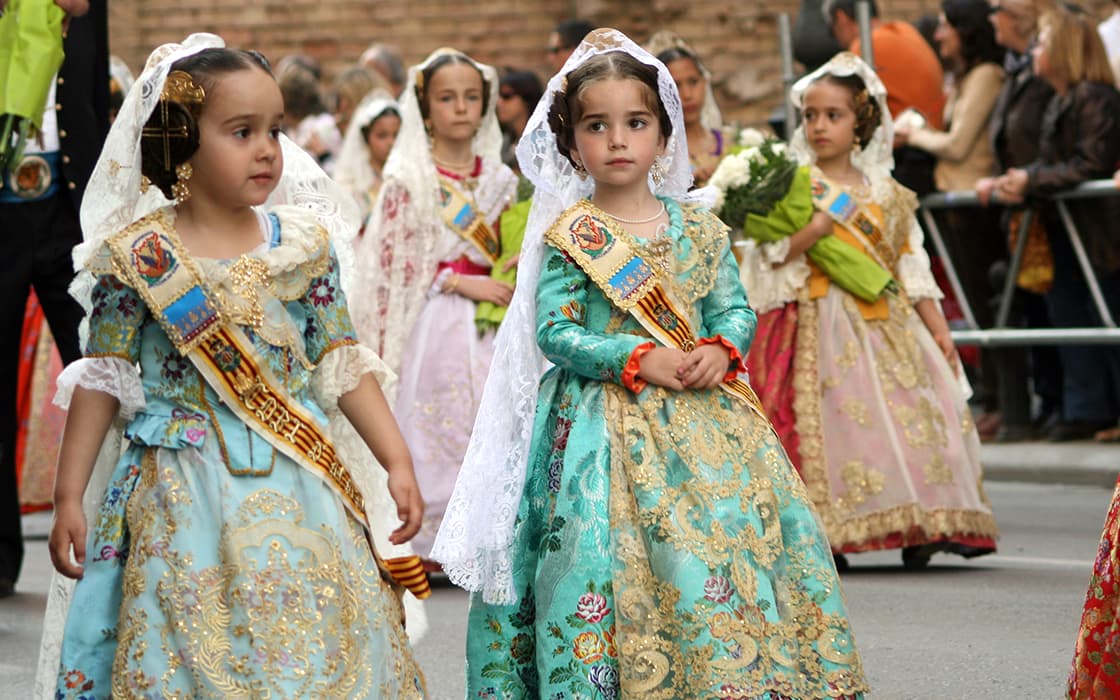 Junge Mädchen in farbenfrohen spanischen Kleidern und Spitzenschleiern ziehen fröhlich umher und feiern die Tradition in Costa Azahar, Spanien.