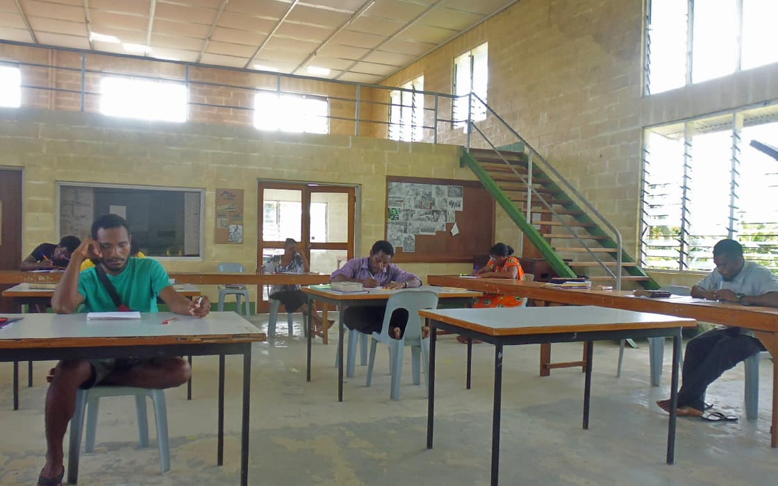 Im Klassenzimmer des Bibeltrainingszentrums sitzen mehrere Studenten an auseinander stehenden Tischen und konzentrieren sich auf ihre Prüfungen.
