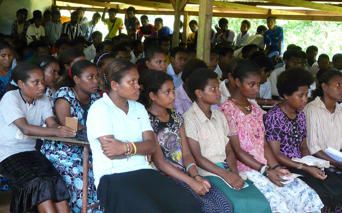 Eine Gruppe sitzt aufmerksam in Reihen unter einem Unterstand in einem Bibelschulungszentrum in Papua-Neuguinea.