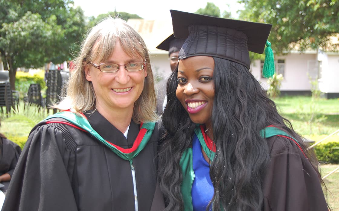 Zwei Frauen in Talar und Mütze lächeln bei der Abschlussfeier an der Evangelischen Universität in Sambia im Freien.