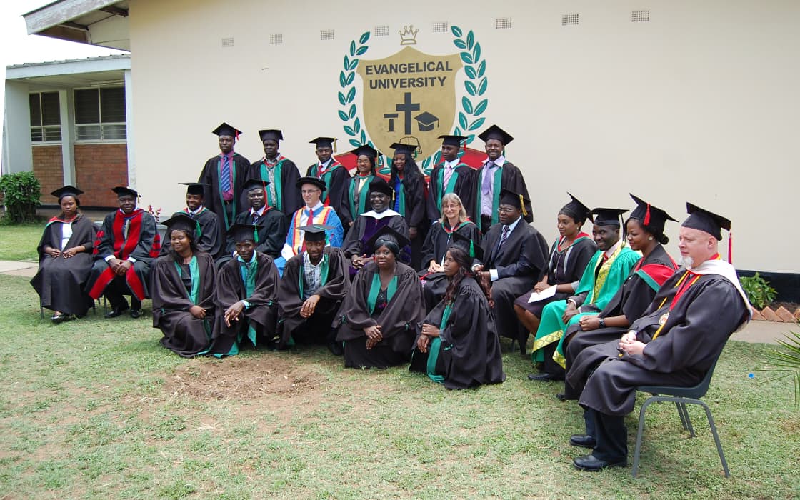 Eine Gruppe von Absolventen und Dozenten in Kappen und Talaren posiert für ein Foto vor der Evangelischen Universität in Sambia.