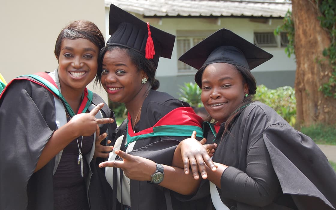 Drei Frauen in Talar und Mütze feiern ihren Abschluss an der Evangelischen Universität in Sambia.
