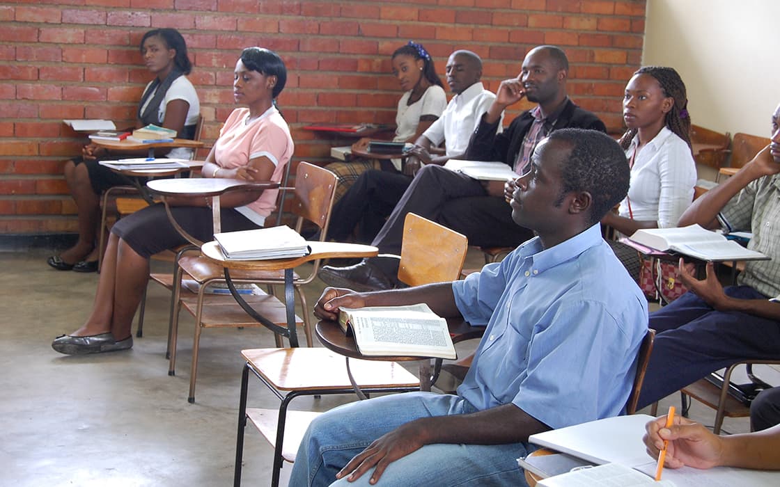 Eine Gruppe von Studenten der Evangelischen Universität in Sambia sitzt in einem Klassenzimmer und hört aufmerksam einer Unterrichtsstunde zu.
