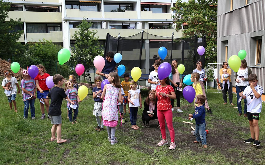 Kinder und Erwachsene stehen auf einer Wiese und halten bunte Luftballons bei einem Treffen der Gruppe Hoffnungshaus Bad Liebenzell in Deutschland.