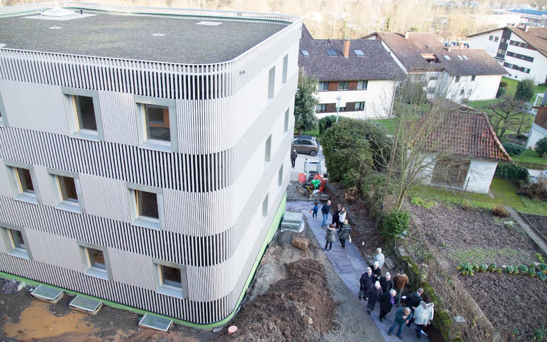 Eine Gruppe von Menschen geht einen Weg am Hoffnungshaus entlang, einem modernen Gebäude in Bad Liebenzell, Deutschland.