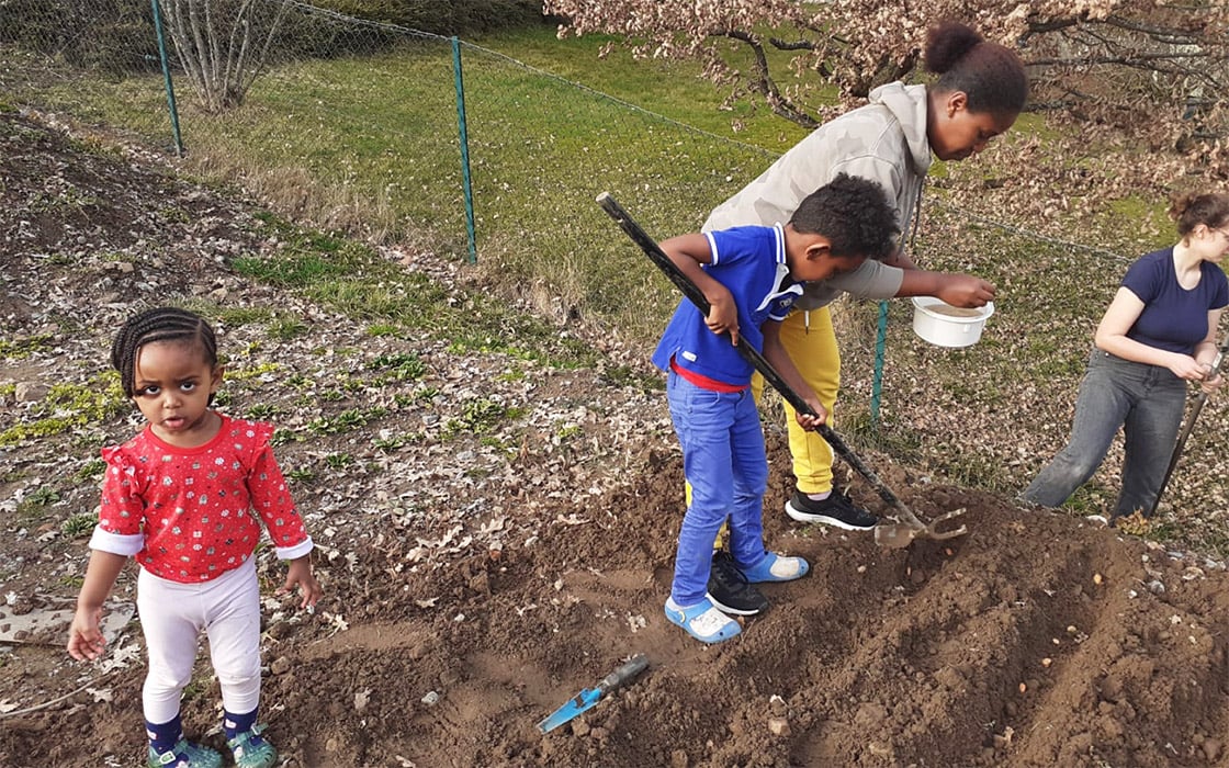 Drei Kinder und ein Erwachsener pflanzen Samen in einem Garten im Hoffnungshaus Bad Liebenzell; ein Mädchen steht daneben und schaut zu.
