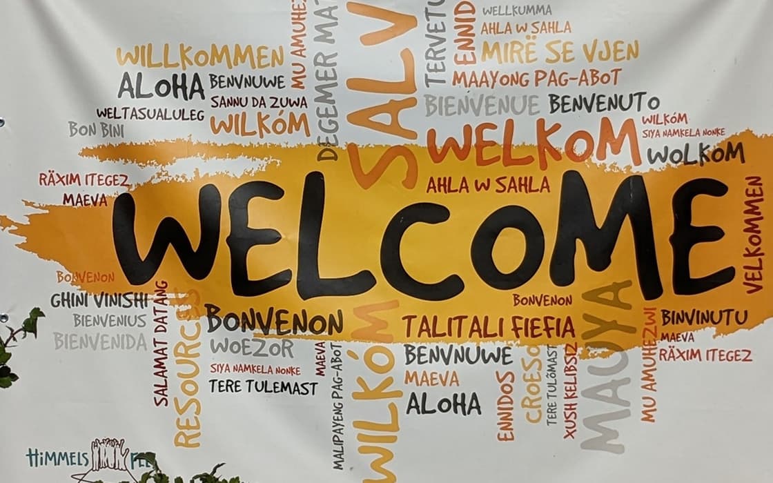 Willkommen in großen schwarzen Buchstaben, Integration und Willkommen in vielen Sprachen auf weißem und gelbem Hintergrund.