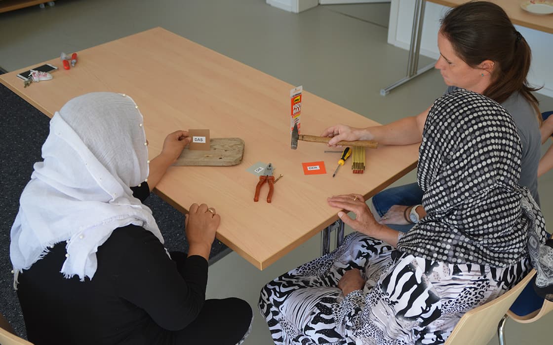 Zwei Frauen sitzen an einem Tisch in Deutschland und arbeiten an einem Handwerksprojekt mit kleinen Werkzeugen; eine Frau hält einen Hammer.