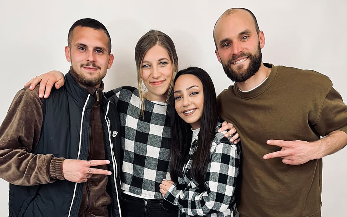 Vier Menschen lächeln in die Kamera, zwei machen Friedenszeichen und zeigen damit ihre Mission der Integration in Deutschland.