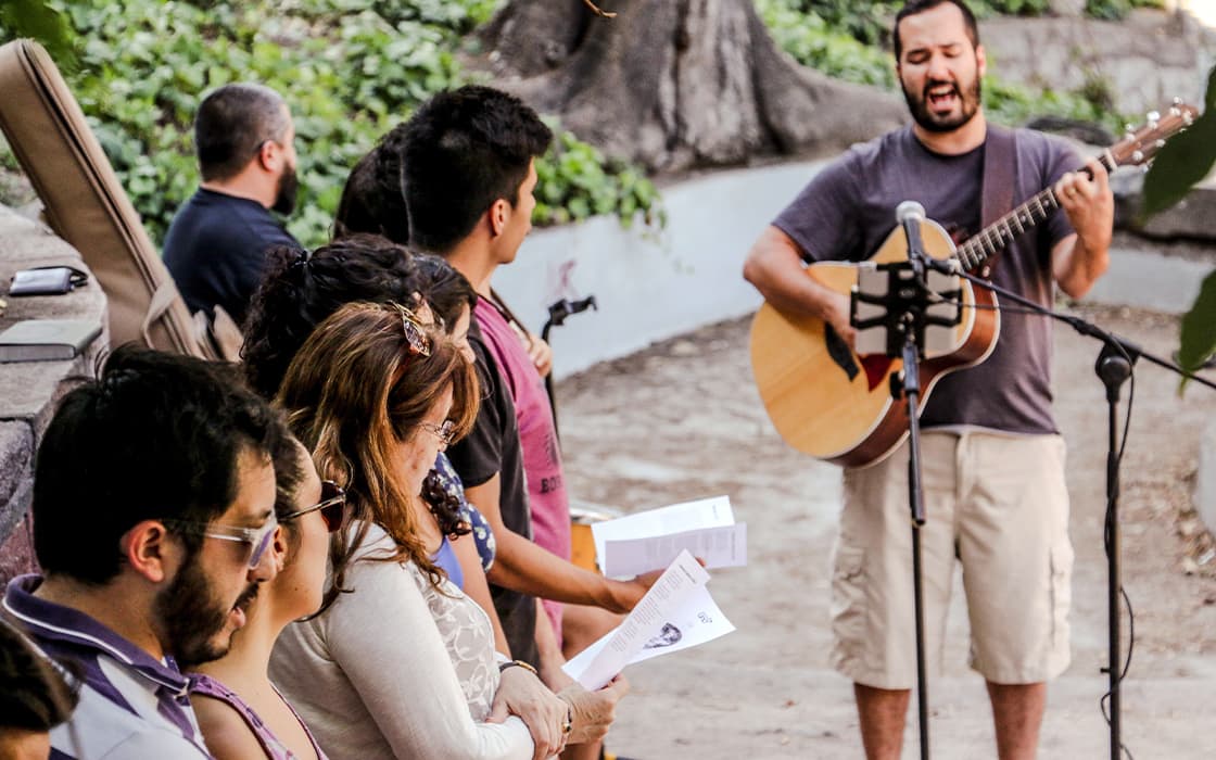 Ein Mann spielt Gitarre und singt im Freien in Chile, während eine Gruppe mit Liedblättern in der Hand mitsingt - Mobilisierung in Aktion.