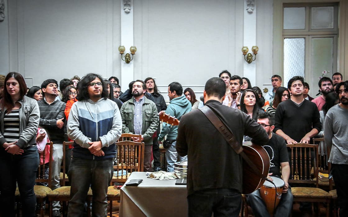 Eine Gruppe blickt nach vorne, während Musiker in einem gut beleuchteten Raum mit Holzstühlen in Chile Gitarren spielen.