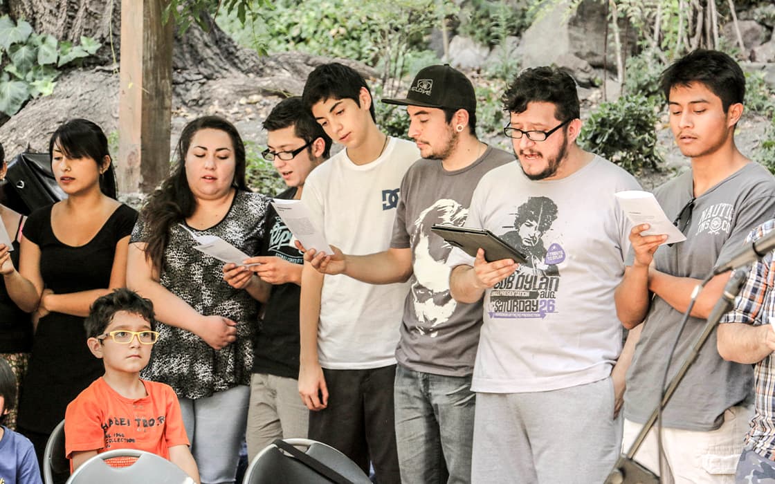 Eine Gruppe in Chile steht im Freien in einer Reihe, hält Papiere in der Hand und singt Mission Mobilizing, während ein Kind zusieht.