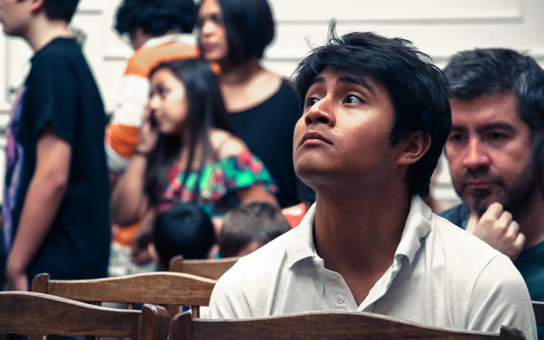 Ein Mann in einem weißen Hemd blickt nachdenklich auf, während andere im unscharfen Hintergrund stehen und reden, konzentriert auf die Mission Mobilizing.