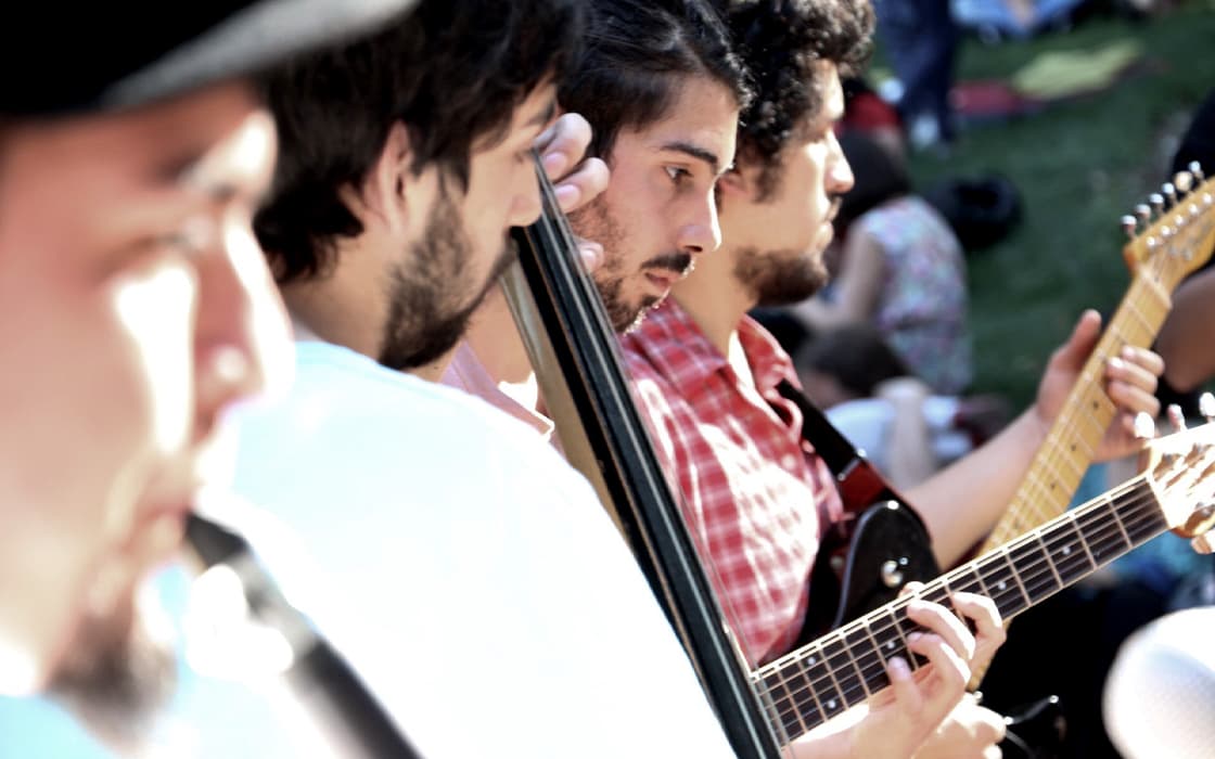 Vier Männer in Chile, die im Freien Gitarre und Blasinstrumente spielen und vor einer Menschenmenge im Hintergrund für die Mission mobilisieren.