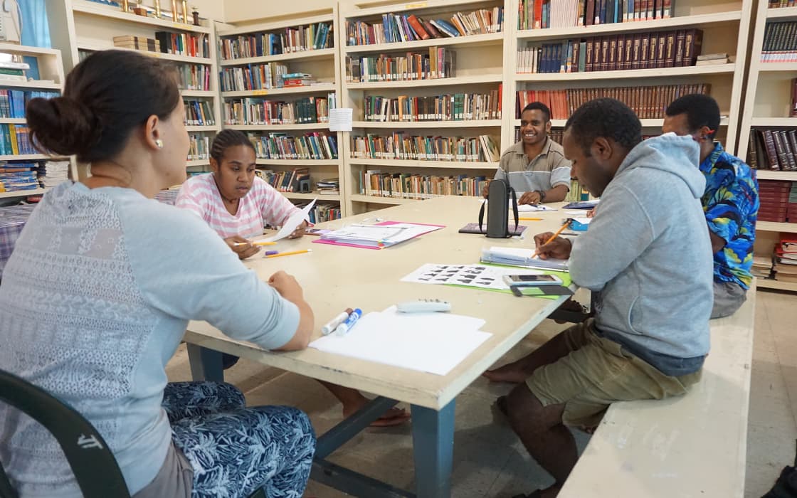Fünf Personen studieren und schreiben gemeinsam an der Pacific Islands University, umgeben von Bücherregalen in Mikronesien.