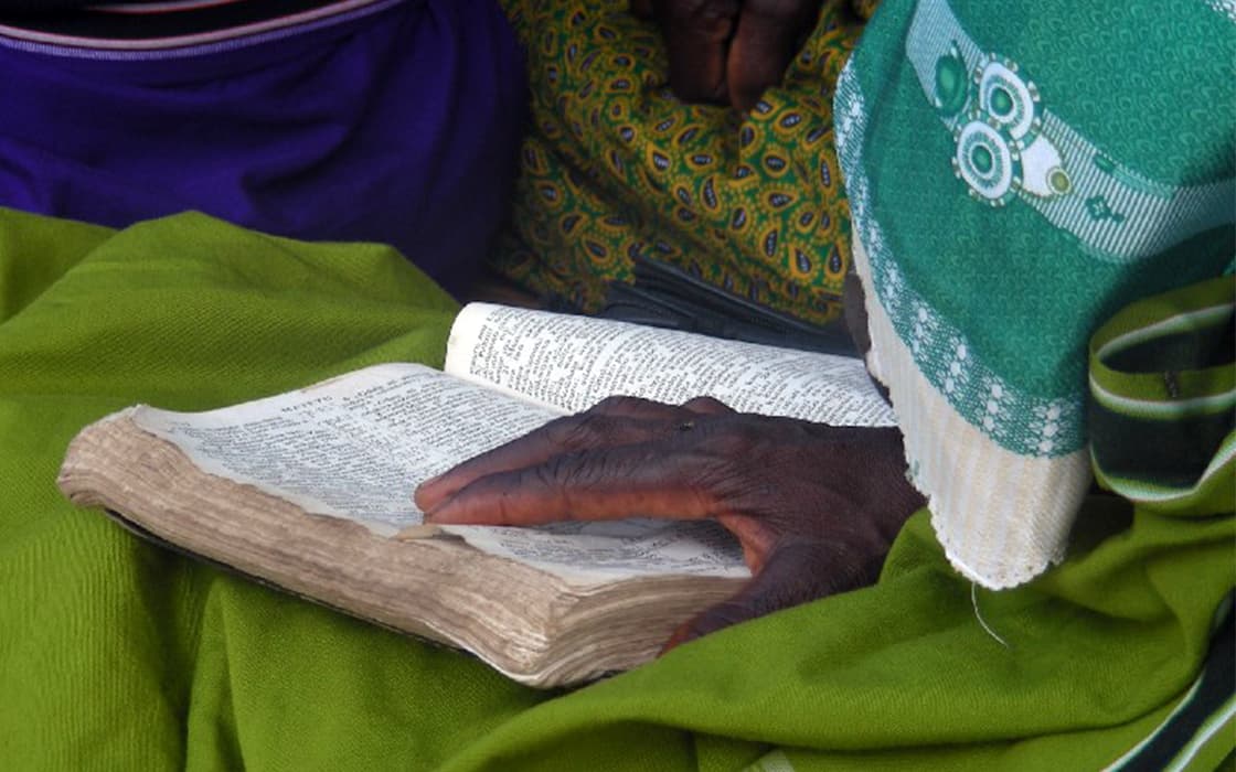 Eine Person mit grünem Kopftuch liest in einem alten Buch und berührt sanft die Seiten - verloren in Geschichten aus Malawi.