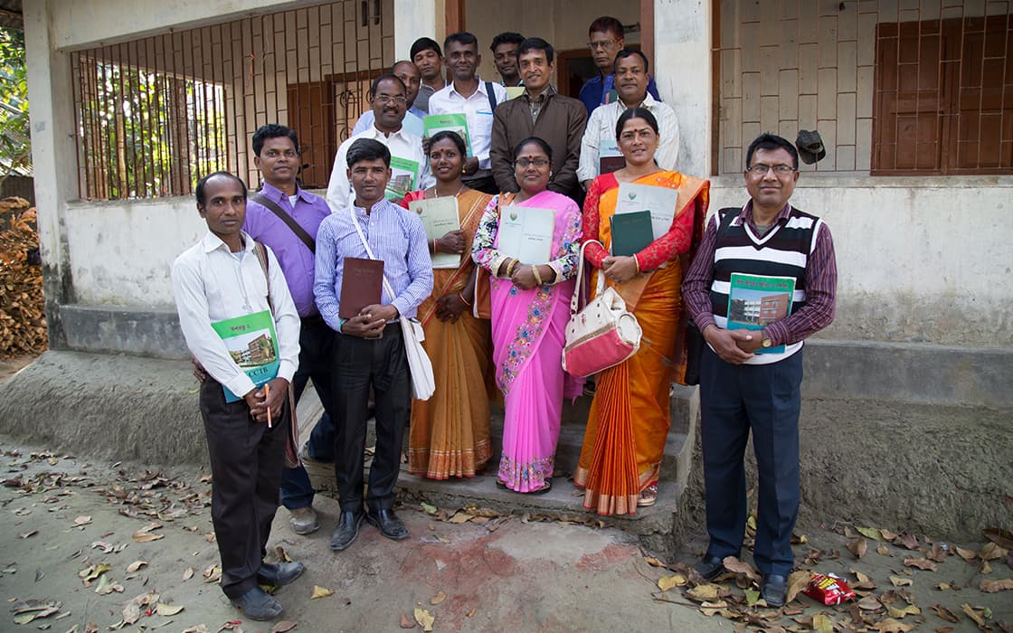 Eine Gruppe in traditioneller Kleidung steht draußen und lächelt mit Büchern - Studenten der TEE Bangladesch Theologische Ausbildung.