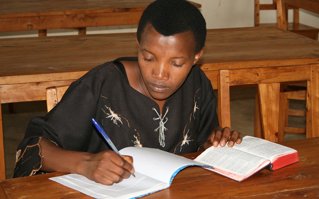 Eine Person sitzt an einem hölzernen Schreibtisch und schreibt in ein Notizbuch - TEE Burundi unterstützt die außerschulische Ausbildung im Klassenzimmer.