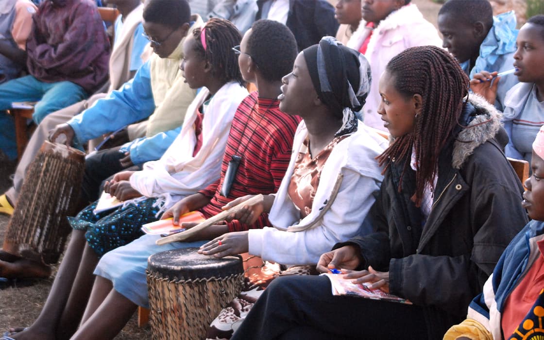 Eine Gruppe junger Menschen, die im Freien trommeln und Hefte in der Hand halten, absolviert eine außerschulische theologische Ausbildung.