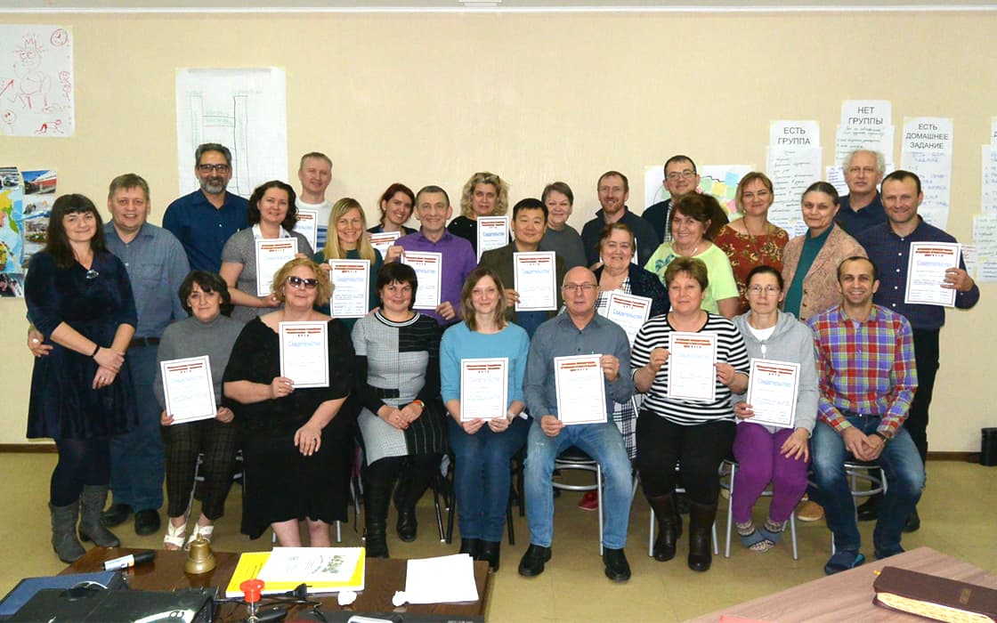 Eine Gruppe Erwachsener in Russland posiert in einem Haus, hält ihre Zertifikate für ihre theologische Ausbildung in der Hand und lächelt.