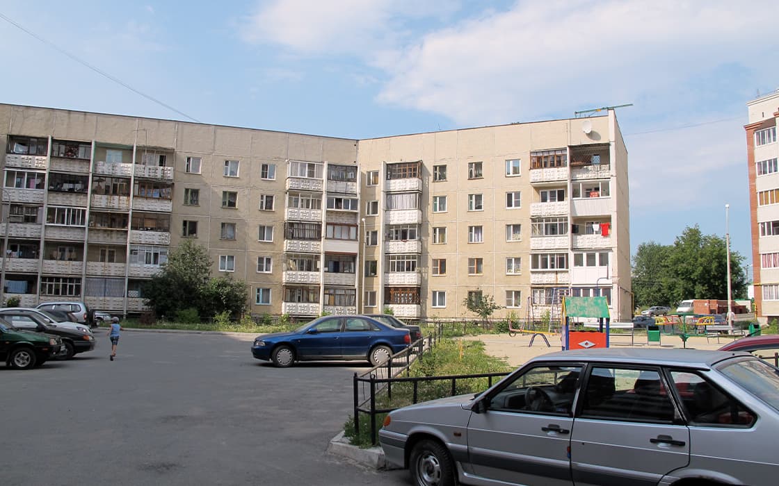 Ein Wohnhaus aus der Sowjetzeit in Russland mit Balkonen, geparkten Autos und Menschen, die im Innenhof spazieren gehen.