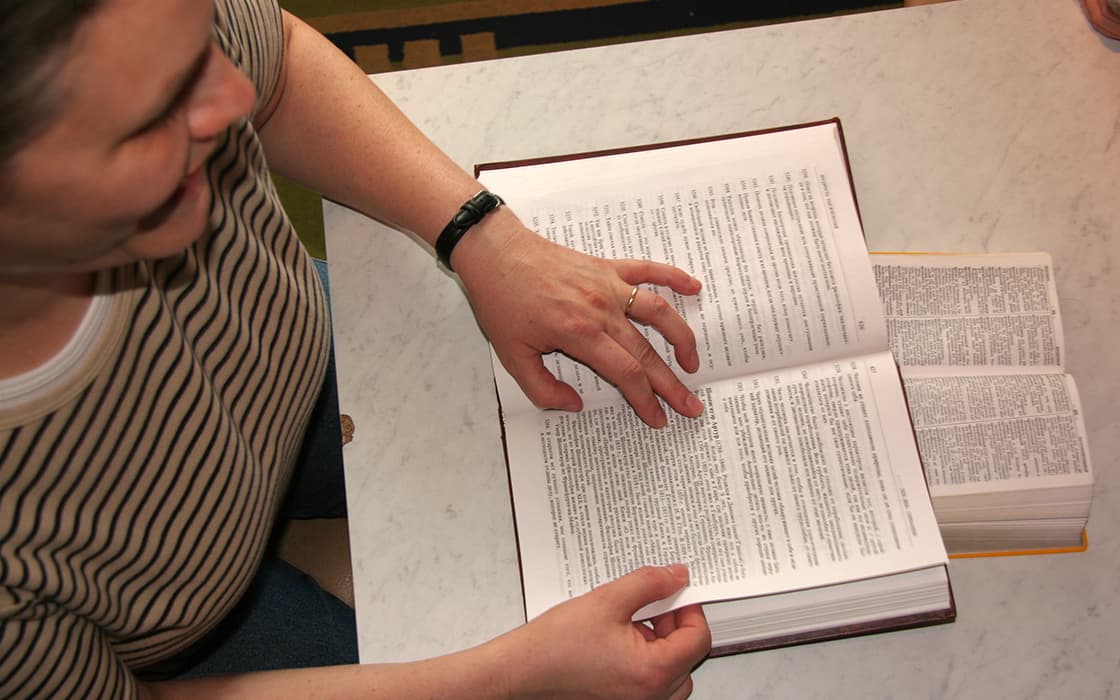 Person im gestreiften Hemd liest über TEE Russland und zeigt auf einen Text in einem aufgeschlagenen Buch über theologische Ausbildung.