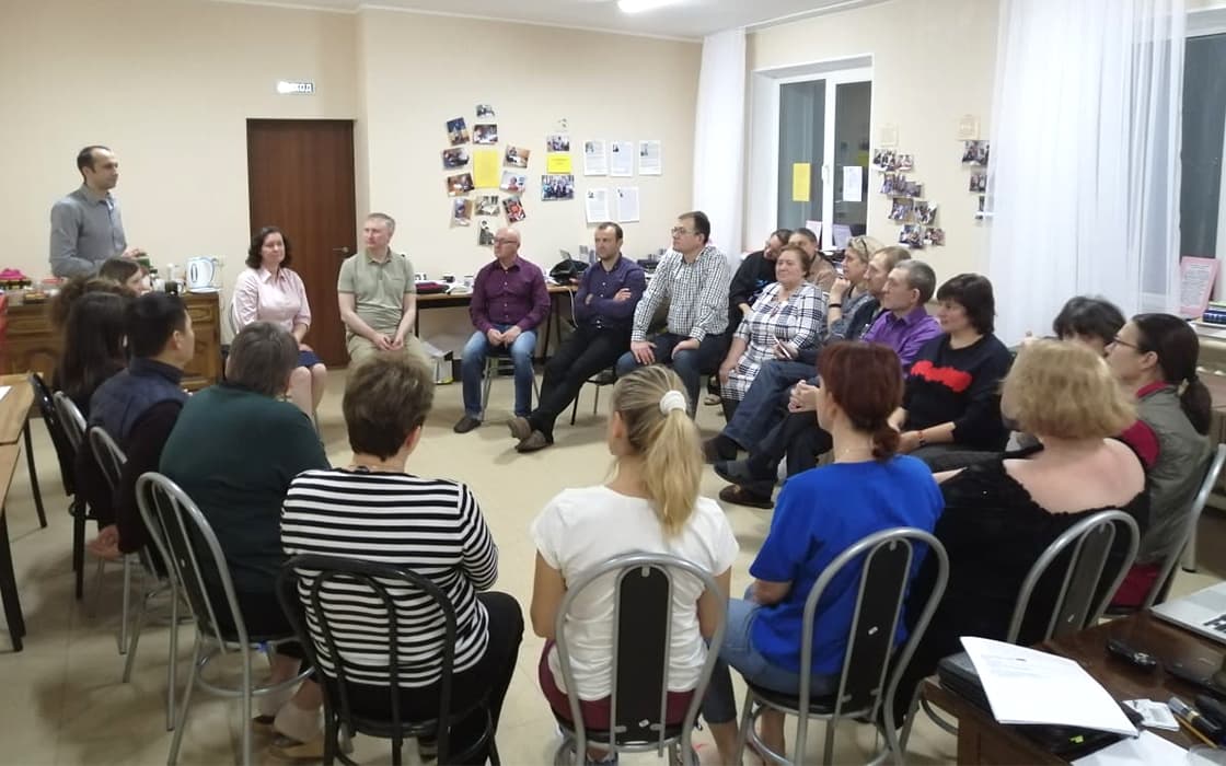 Eine Gruppe diskutiert über die theologische Ausbildung in Russland und hört einem Mann zu, der vorne in einem hellen Raum sitzt.