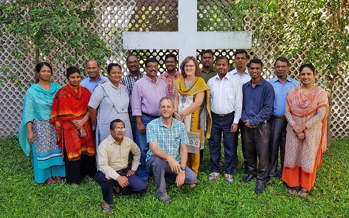 Eine Gruppe versammelt sich vor einem großen Kreuz und einer gemusterten Wand am College of Christian Theology Bangladesh.
