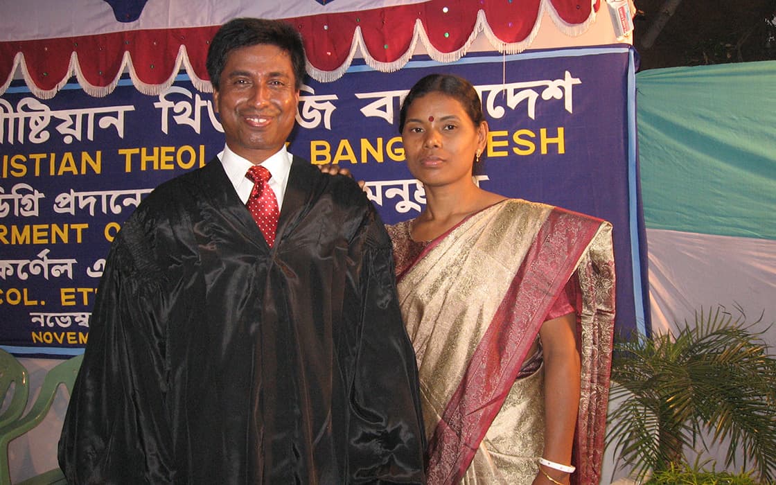 Ein Mann in einer schwarzen Abschlussrobe steht neben einer Frau in einem Sari bei einer Veranstaltung des Bangladesh Theology College.