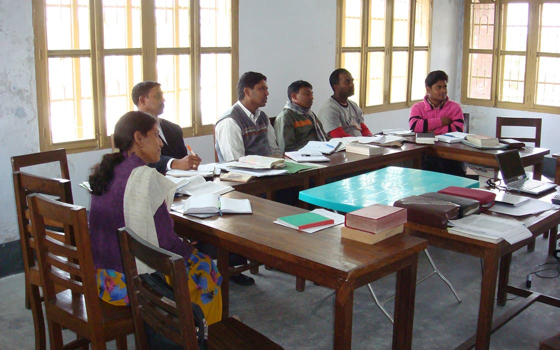In einem Klassenzimmer der Hochschule für Christliche Theologie sitzen sechs Personen an Tischen, mit aufgeschlagenen Büchern, vor großen Fenstern um einen Laptop versammelt.