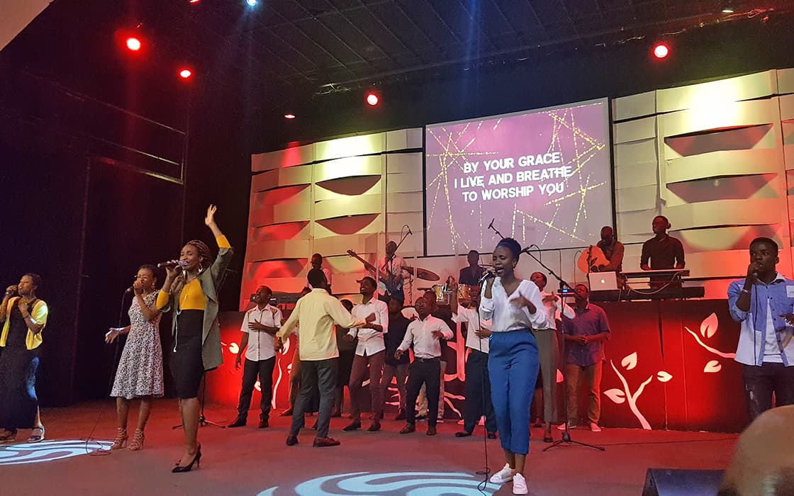 Eine Gruppe von Sängern und Musikern tritt auf der Bühne auf, wobei die Texte der Anbetung angezeigt werden, um die Bemühungen der Gemeindegründungen zu unterstützen.