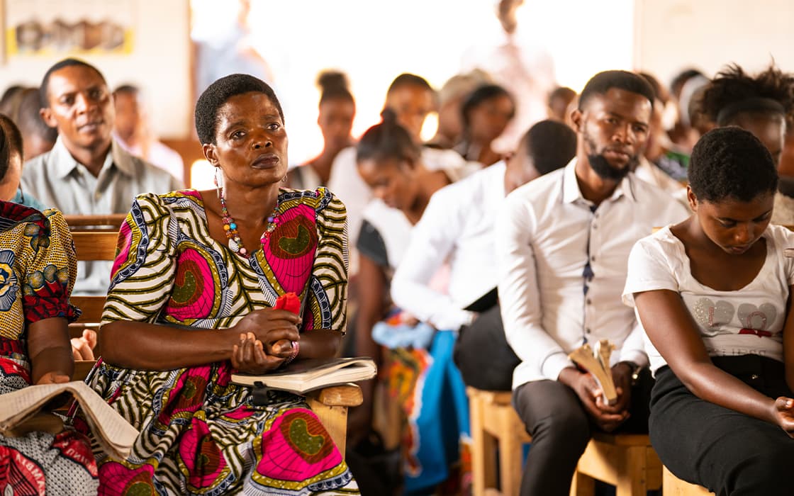 Dicht beieinander sitzende Menschen, die in einem hell erleuchteten Raum aufmerksam zuhören - vielleicht bei einer Veranstaltung von Gemeindegründungen in Sambia.