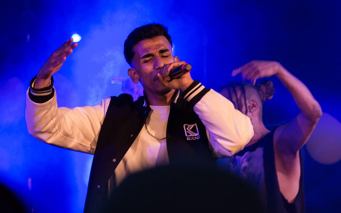 Ein Sänger, der mit einem Mikrofon auf der Bühne steht, beleuchtet von blauen und lila Lichtern bei Lubu Beatz in Deutschland.