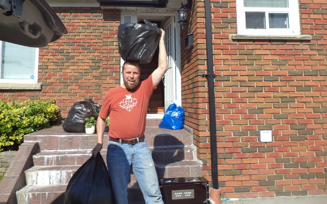 Ein Mann in einem roten Hemd hält Müllsäcke vor einem Backsteinhaus in Toronto und steht auf einer Treppe mit weiteren Säcken in der Nähe.