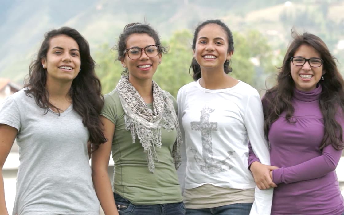 Vier junge Frauen in Ecuador lächeln in die Kamera und zeigen die Jugendarbeit Ecuador inmitten von Bergen und Grün.