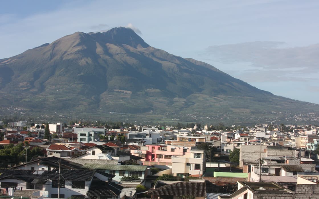 Städtische Gebäude mit einem großen grünen Berg im Hintergrund - perfekt für Projekte der Jugendarbeit Ecuador.
