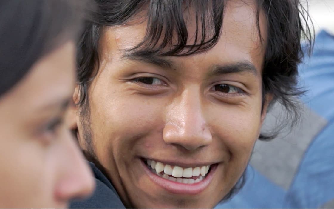 Ein junger Mann mit dunklen Haaren lächelt herzlich und unterhält sich mit einer Person im Vordergrund über Jugendarbeit in Ecuador.