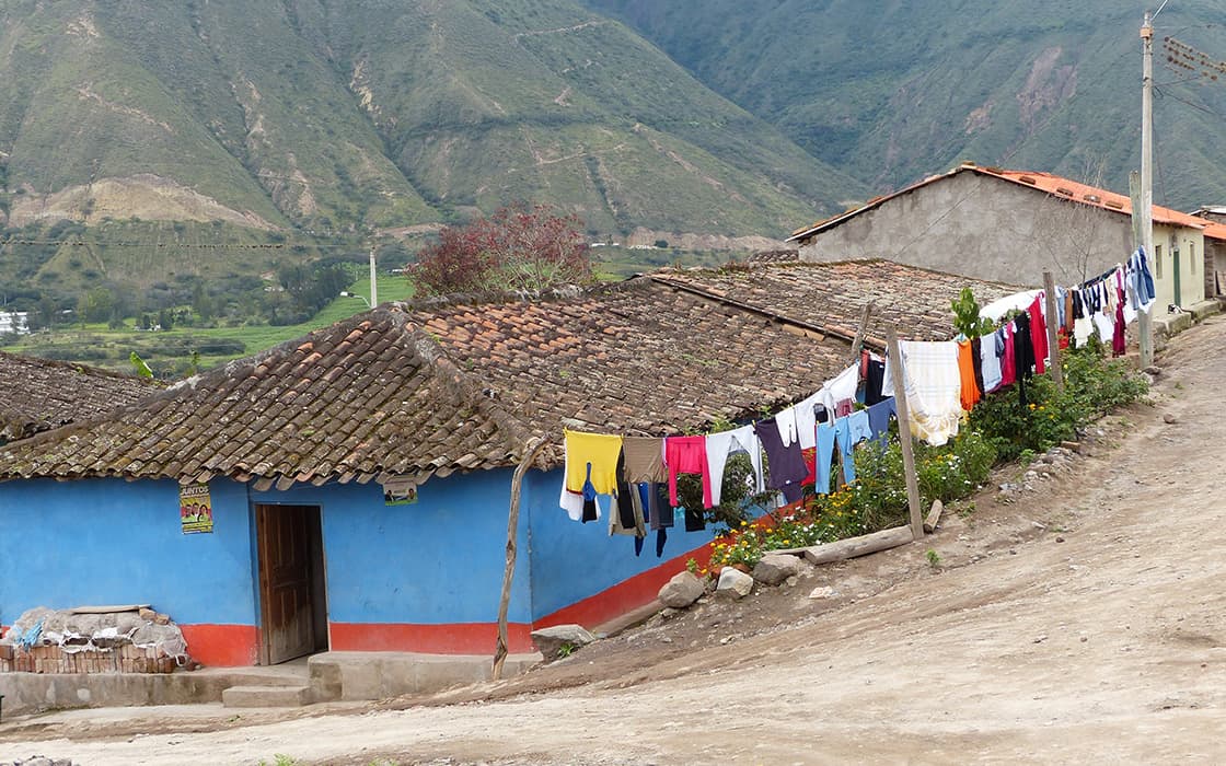 Eine Reihe von Häusern mit Wäsche auf der Leine in der Nähe von Casa Ágape Ecuador, vor der Kulisse grüner Berge und einer unbefestigten Straße.