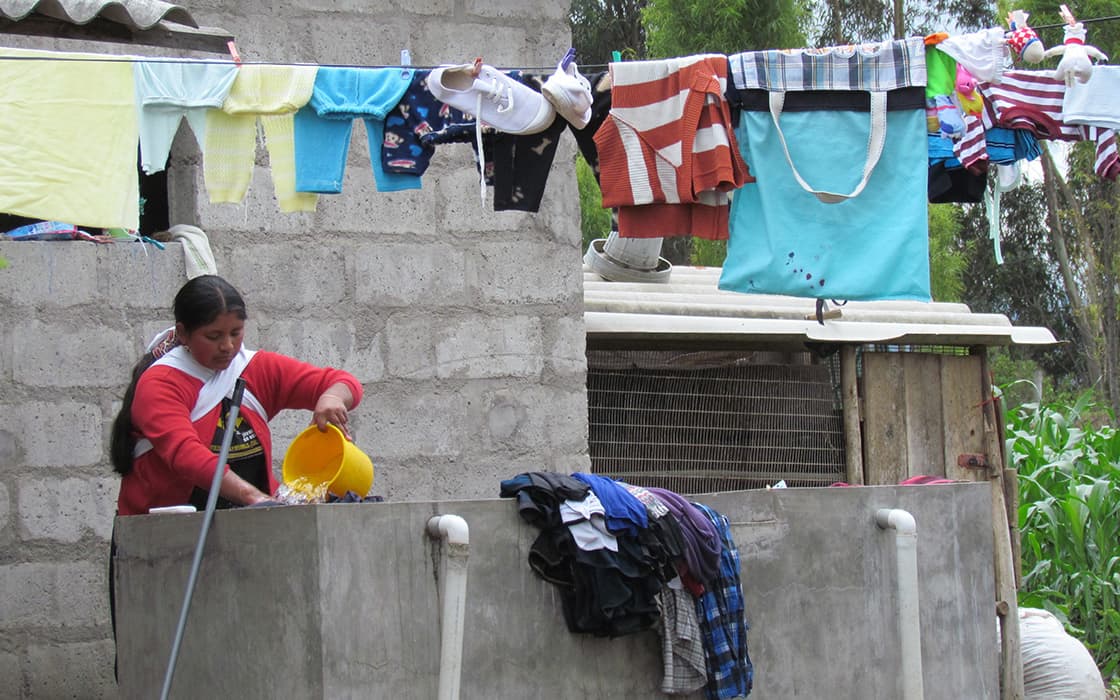 Eine Frau wäscht in Casa Ágape Ecuador ihre Wäsche von Hand, während über ihr die Wäsche auf einer Wäscheleine hängt.