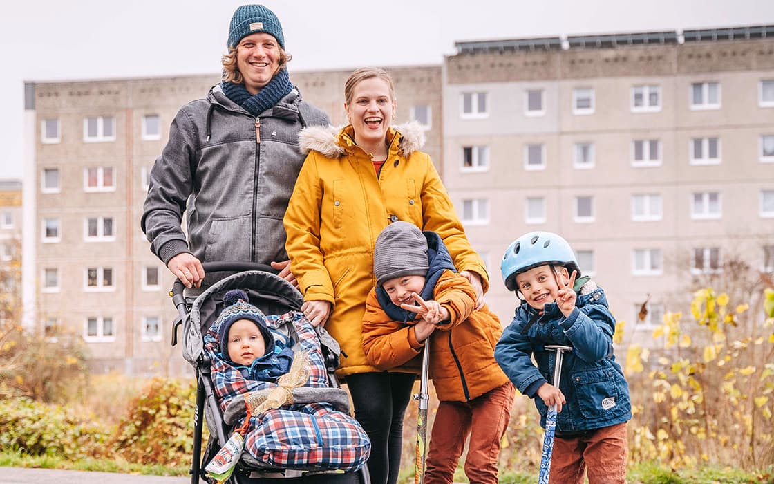 Eine lächelnde Familie mit drei Kindern, eines davon in einem Kinderwagen, posiert im Freien in Rostock, Deutschland.