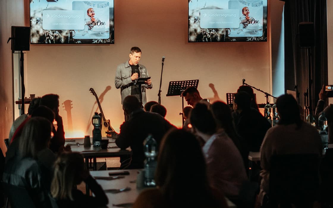 Ein Mann spricht auf der Bühne einer Veranstaltung der Lifepoint Church in Stuttgart, hinter ihm das Publikum und Präsentationsbildschirme.