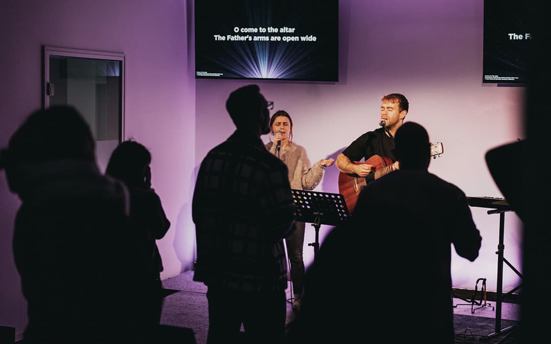 Zwei Musiker stehen in Stuttgart auf der Bühne und singen mit Gitarre, während in der Lifepoint-Kirche Texte projiziert werden.