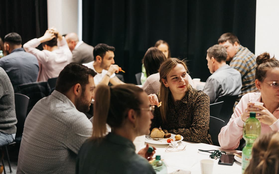 Menschen versammeln sich an Tischen, essen und unterhalten sich bei einer Indoor-Veranstaltung der Lifepoint Church in Stuttgart, Deutschland.