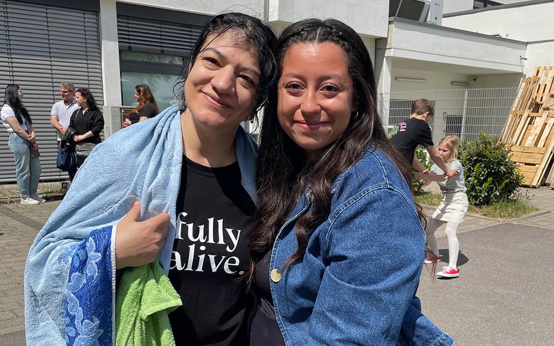 Zwei Frauen lächeln im Freien an der Lifepoint Church Stuttgart, die eine mit nassen Haaren und Handtuch, die andere in Jeansjacke.