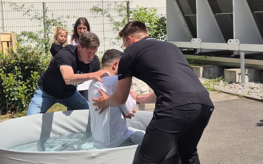 Zwei Männer taufen einen Mann in einer Wanne im Freien in der Lifepoint Church in Stuttgart, während andere in der Nähe zusehen.