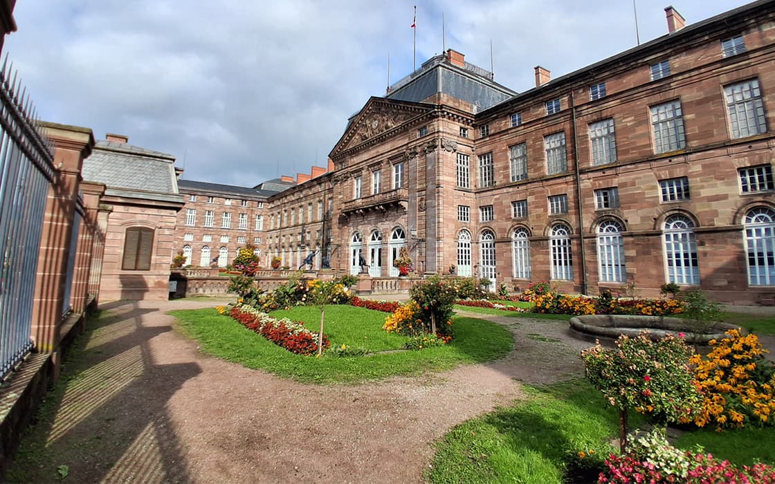 Großes historisches Backsteingebäude mit gewölbten Fenstern, die an Gemeindegründungen in Westfrankreich unter einem bewölkten Himmel erinnern.